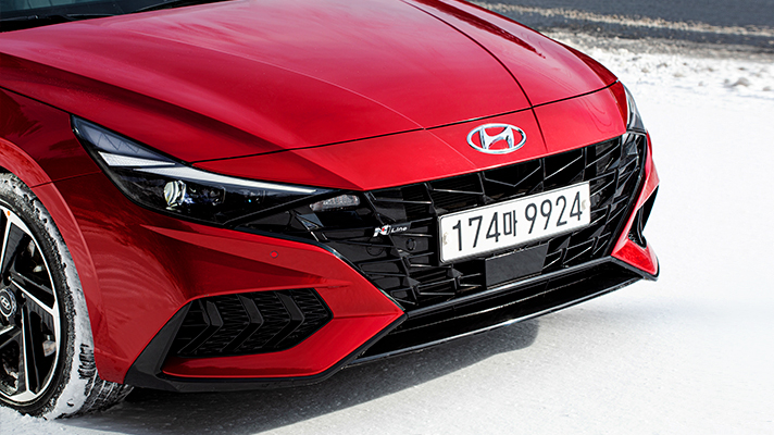 눈길 위에 서 있는 아반떼 N 라인의 라디에이터 그릴과 범퍼의 모습