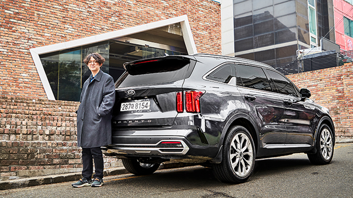 Lee Ho-jin leaning on the back of a parked Kia Sorento