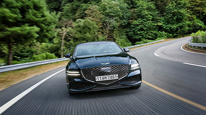 Image of Genesis G80 driving on a road with a forest