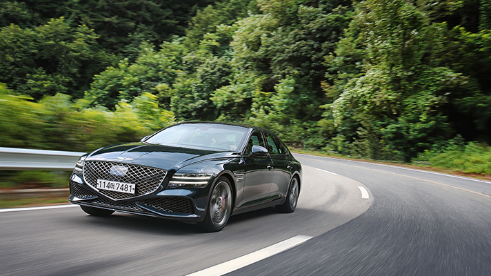Image of Genesis G80 driving on road with forest