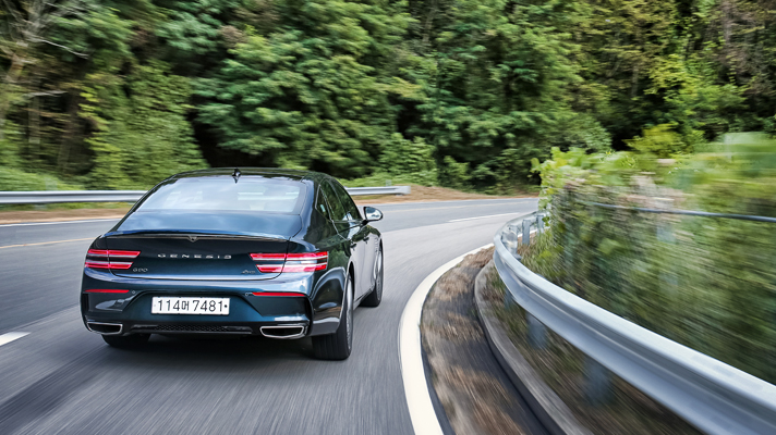 Rear view of Genesis G80 driving on road with forest