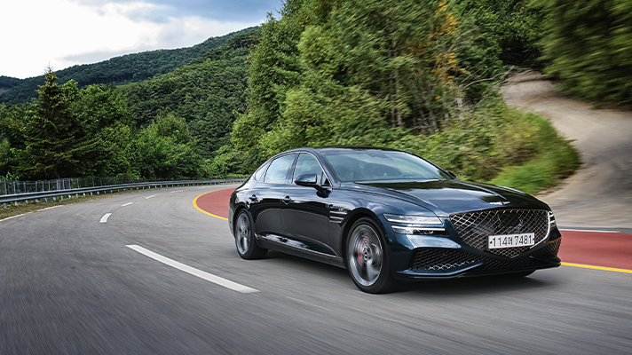 Side view of Genesis G80 driving on a road with a forest