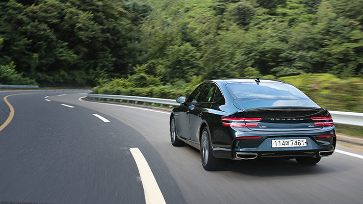 Rear view of Genesis G80 driving on a road with a forest