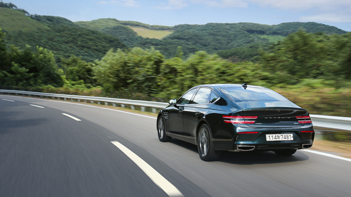 Rear view of Genesis G80 driving on road with forest