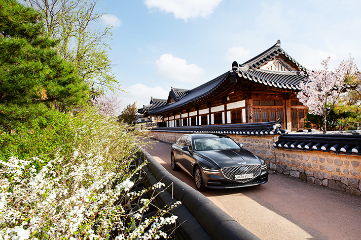 벚꽃이 핀 한옥 앞에 서 있는 제네시스 G80 정면 모습