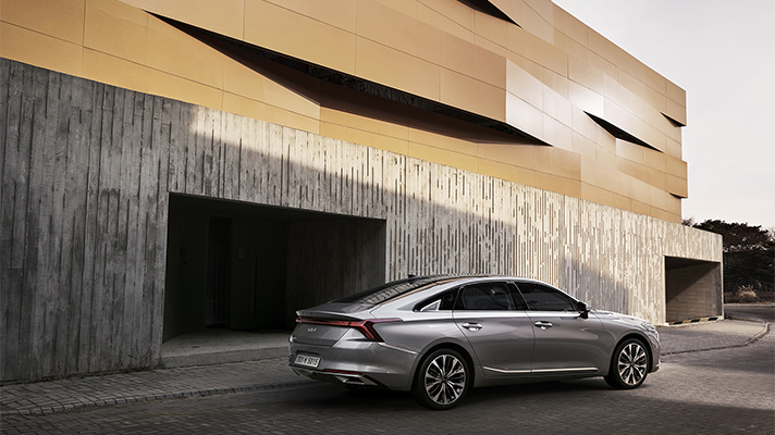 모던 빌딩 앞에 주차된 기아 K8 후면 앵글 모습