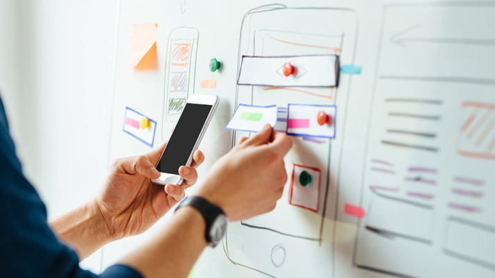 화이트보드 앞에서 핸드폰을 들고 있는 사람