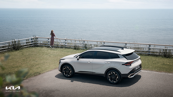 멀리 바다를 내다보는 사람을 배경으로 측면으로 주차된 기아 신형 스포티지