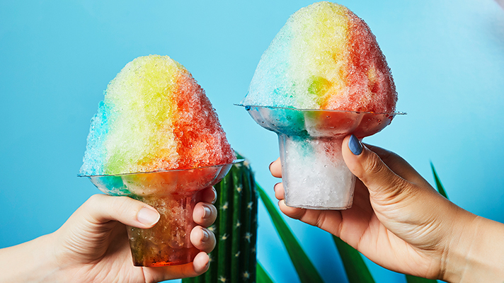 Holding two rainbow iced desserts with blue background