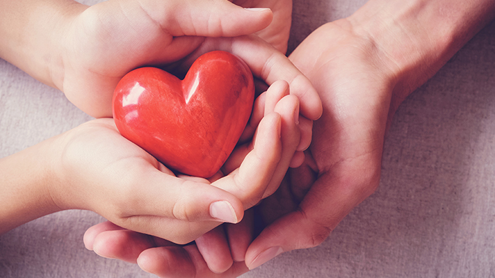 하트 모양의 오브제를 아이와 어른이 양 손으로 감싸듯이 쥐고 있는 모습