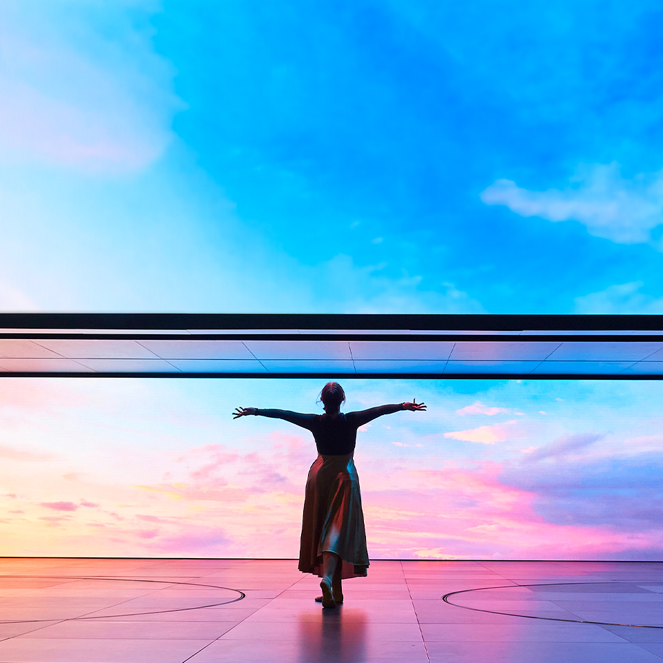 기아의 새로운 로고와 캐치프레이즈가 나와 있는 무대를 배경으로 한 무용수가 춤을 추고 있는 모습