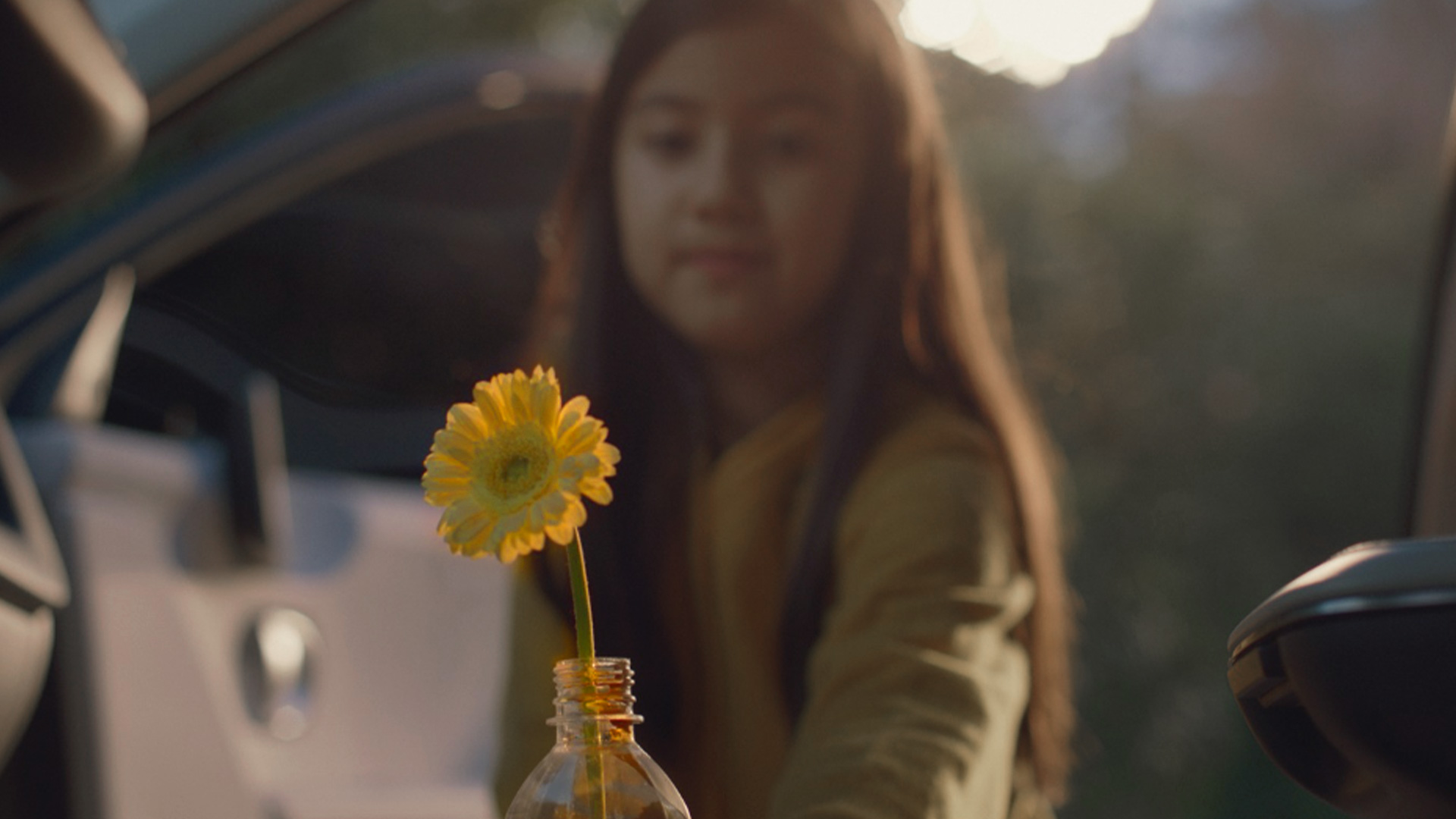 A girl puts yellow flowers in a recycled plastic bottle and puts them in a cupholder of a car
