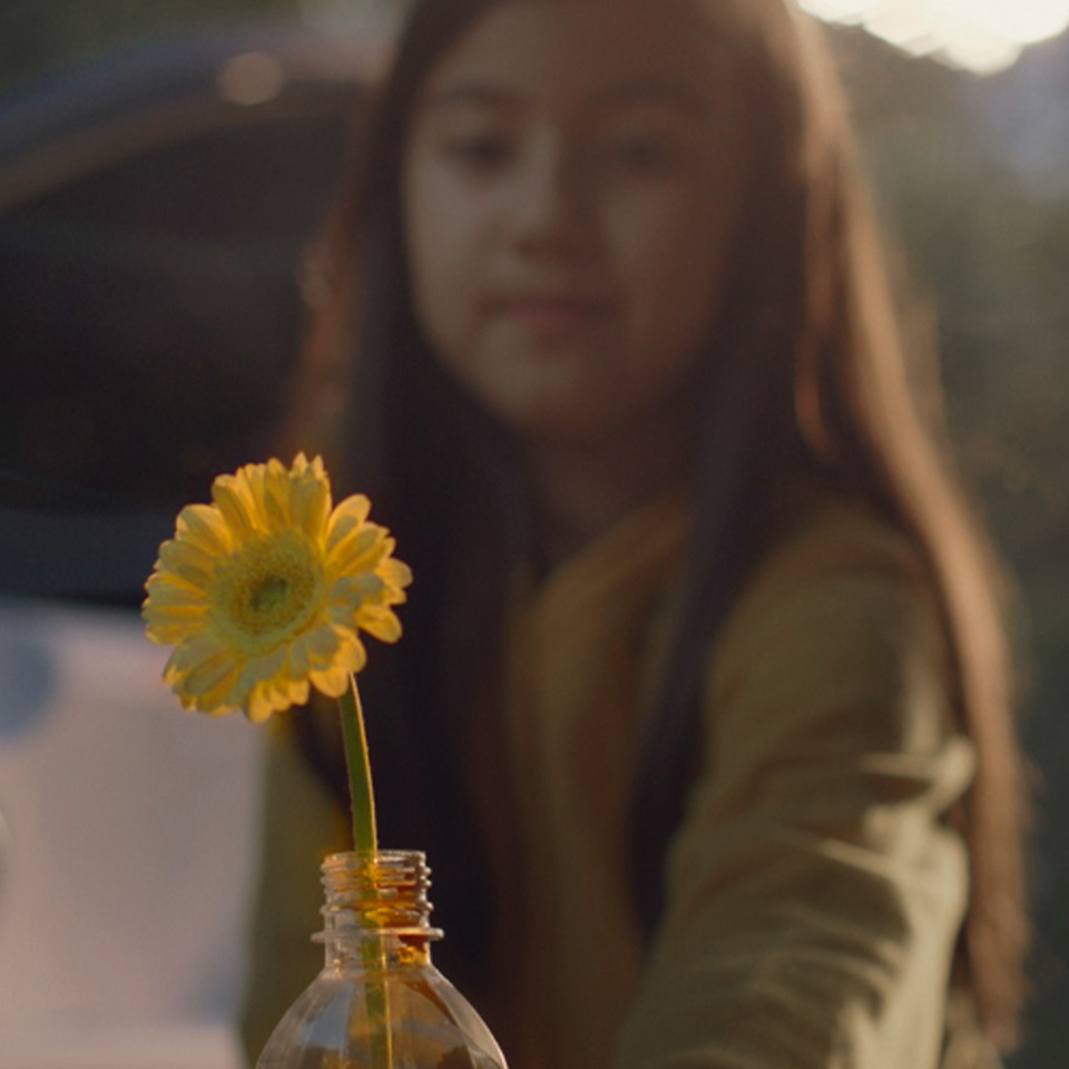 A girl puts yellow flowers in a recycled plastic bottle and puts them in a cupholder of a car