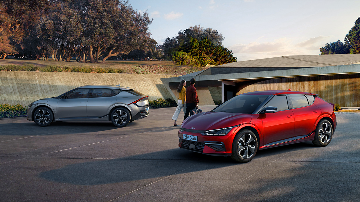 한쌍의 커플이 캐리어를 끌며 두 대의 EV6 사이로 걸어가고 있다