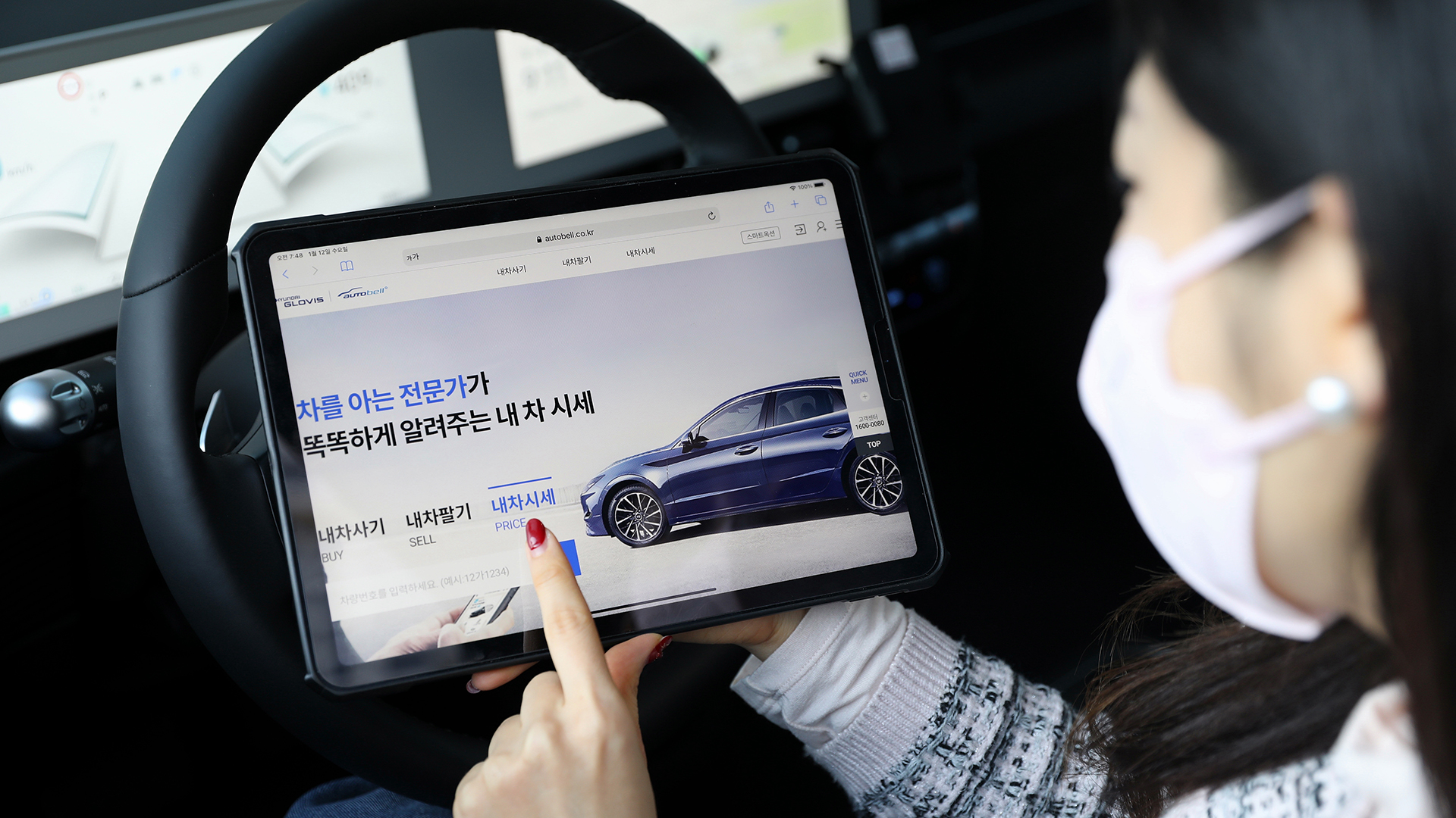 한 여성이 차 안에서 태블릿을 통해 현대글로비스 오토벨의 내 사 시세 서비스를 이용하고 있다