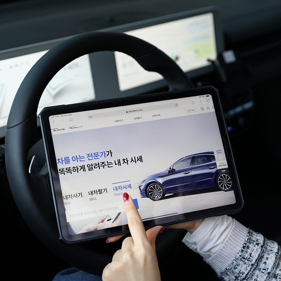 한 여성이 차 안에서 태블릿을 통해 현대글로비스 오토벨의 내 사 시세 서비스를 이용하고 있다