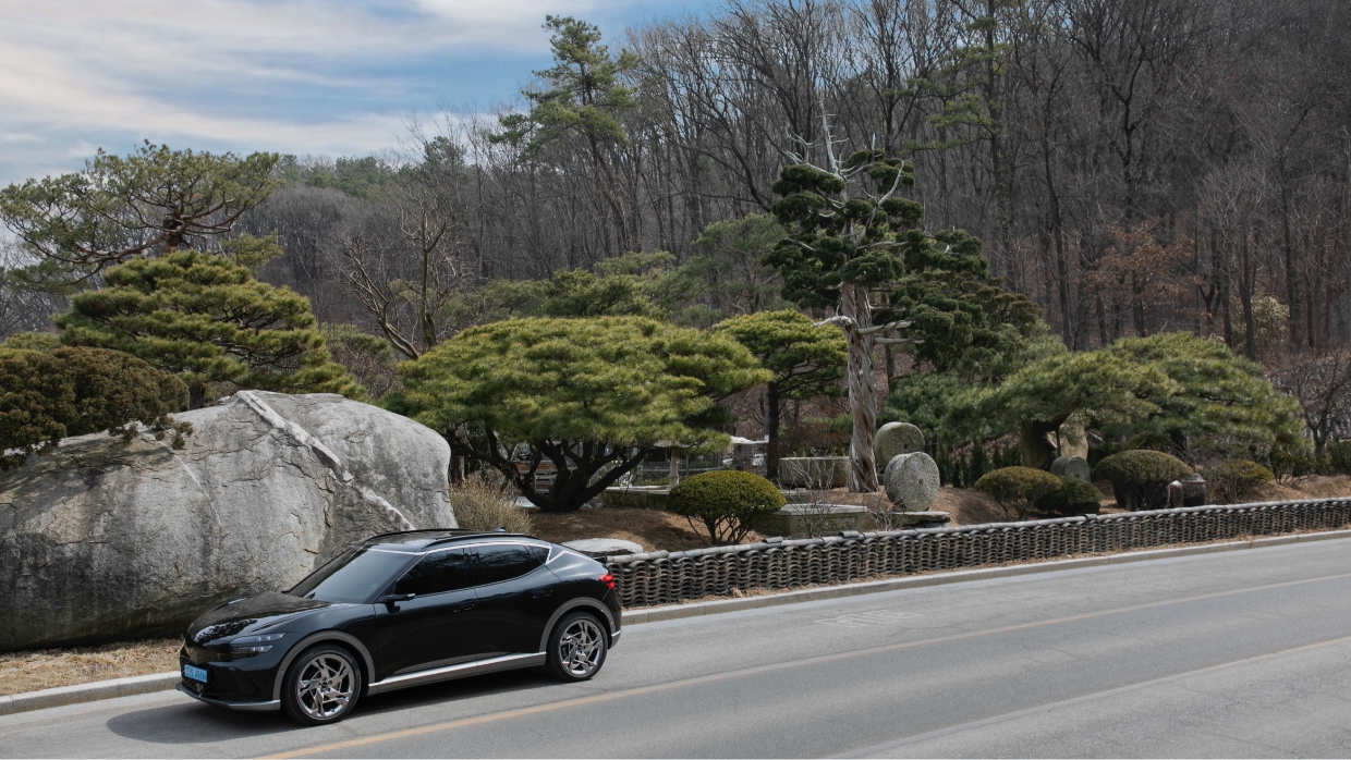 산과 바위를 배경으로 언덕 중턱의 도로를 시원하게 내려오고 있는 GV60의 모습