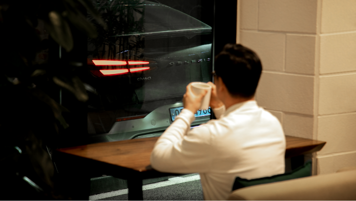 장우영 씨가 카페 창가에 앉아 커피를 마시며 GV60의 뒷모습을 바라보고 있다