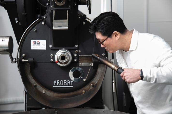 Jang Woo-Young is smelling coffee beans in front of the roasting machine