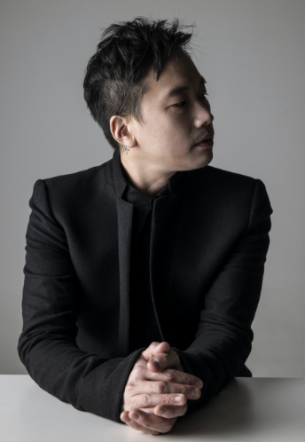음악감독 정재일이 검은 정장을 입은 채 테이블 위로 손을 마주 잡고 측면을 응시한 모습