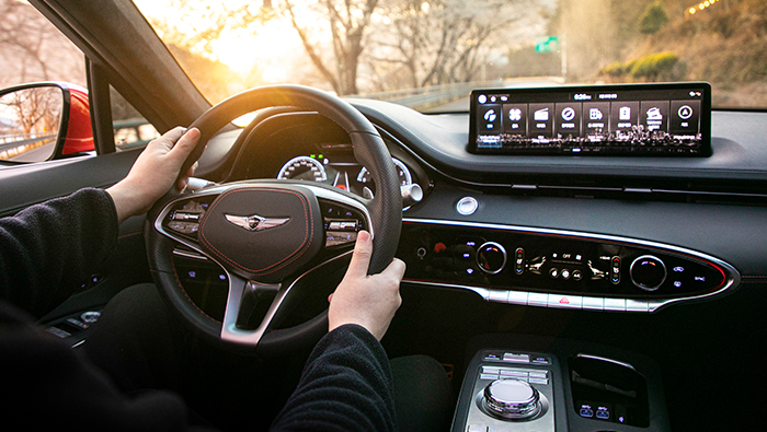 A driver sitting behind the steering wheel of the GV70