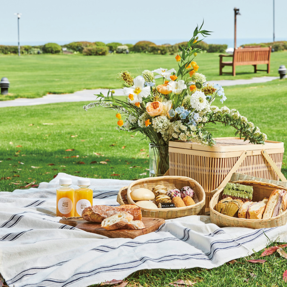 잔디밭에 피크닉 돗자리와 바구니, 식음료가 놓여 있는 모습