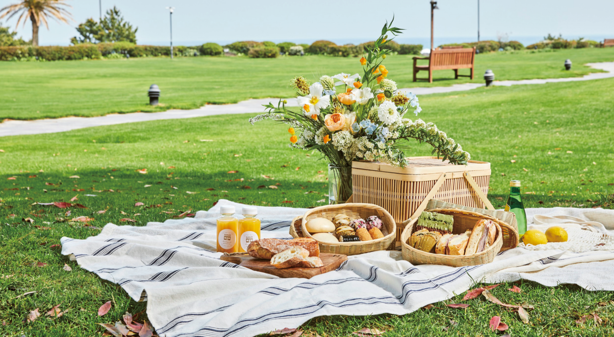 잔디밭에 피크닉 돗자리와 바구니, 식음료가 놓여 있는 모습