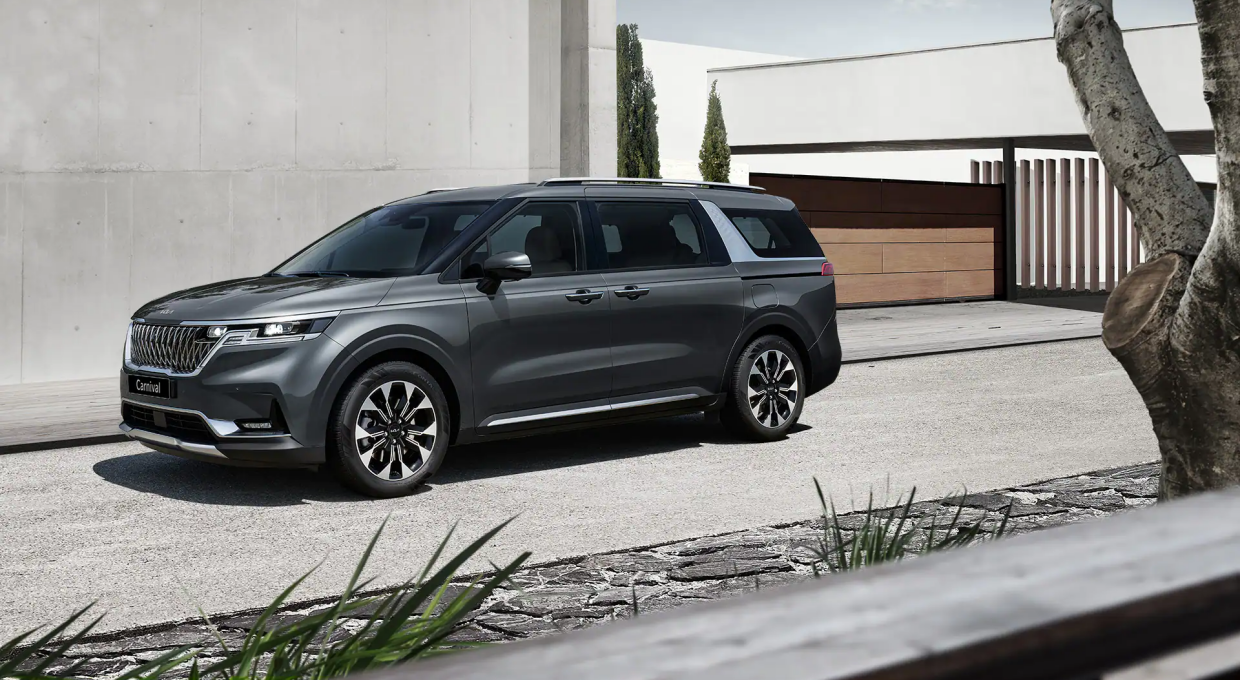 건물 앞에 주차되어 있는 기아 카니발 전측면부 모습