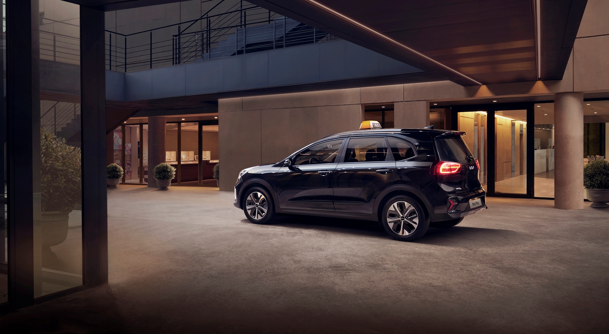 건물 앞에 주차되어 있는 기아 니로 플러스 택시 모델의 후측면부