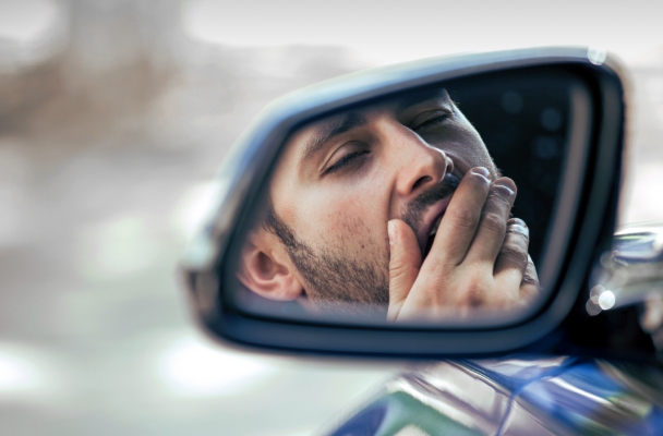 An image of a driver yawning seen through a side mirror