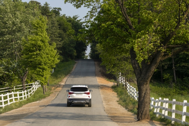 A Kia Seltos is driving down a wooded road