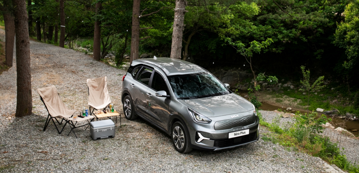 캠핑장에서 캠핑용 의자와 테이블을 펼쳐 놓고 서 있는 니로 플러스의 모습