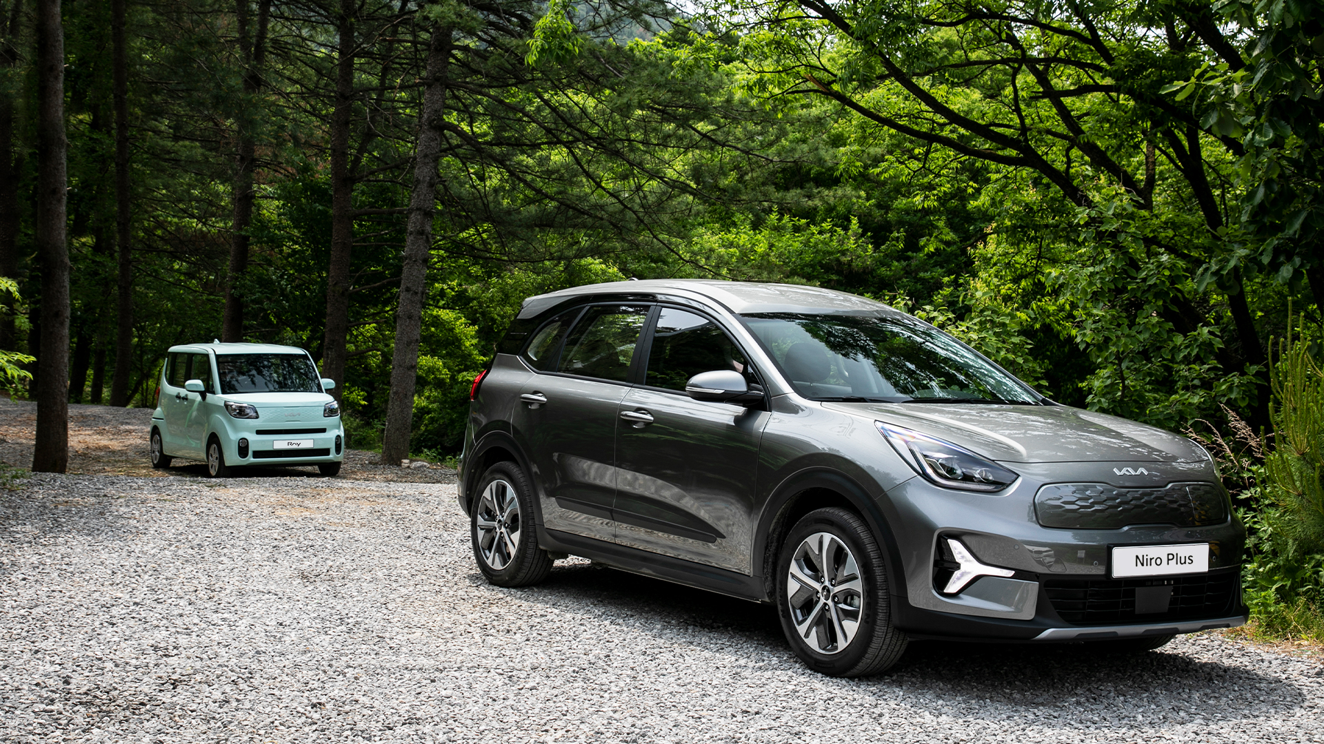 Front side view of single-seater Niro Plus and Ray standing side by side in the forest at the campsite