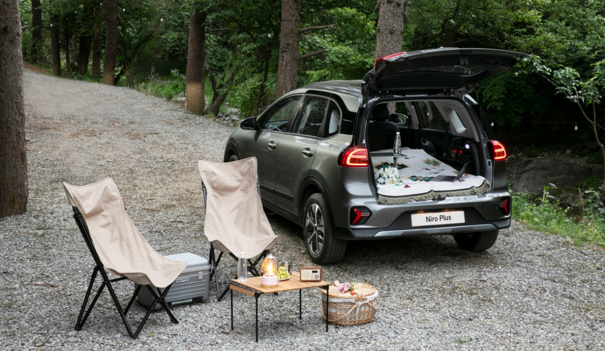 Rear view of Niro Plus standing with a camping chair, table and basket spread out against the forest at the campsite