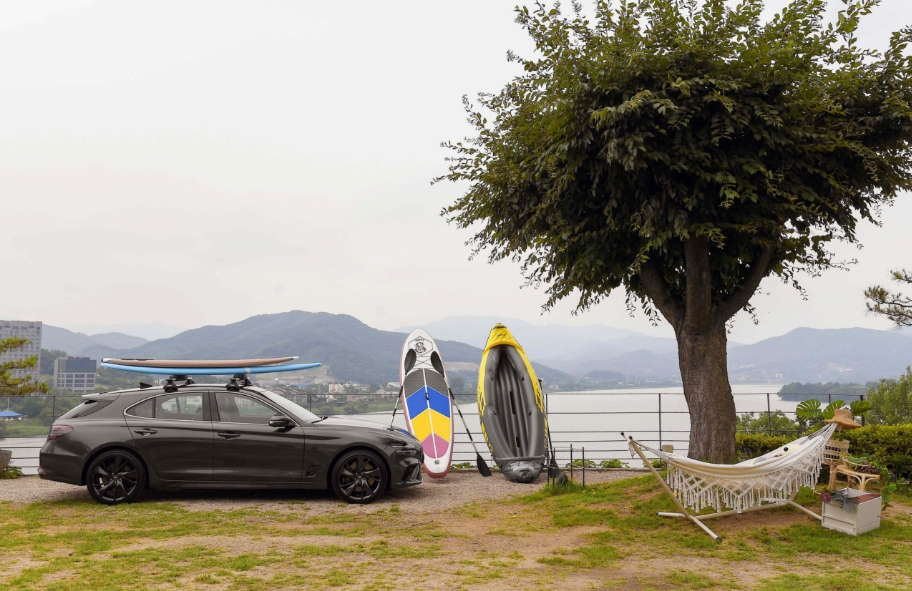 레저와 전원 풍경을 배경으로 서 있는 제네시스 G70 슈팅 브레이크의 옆모습