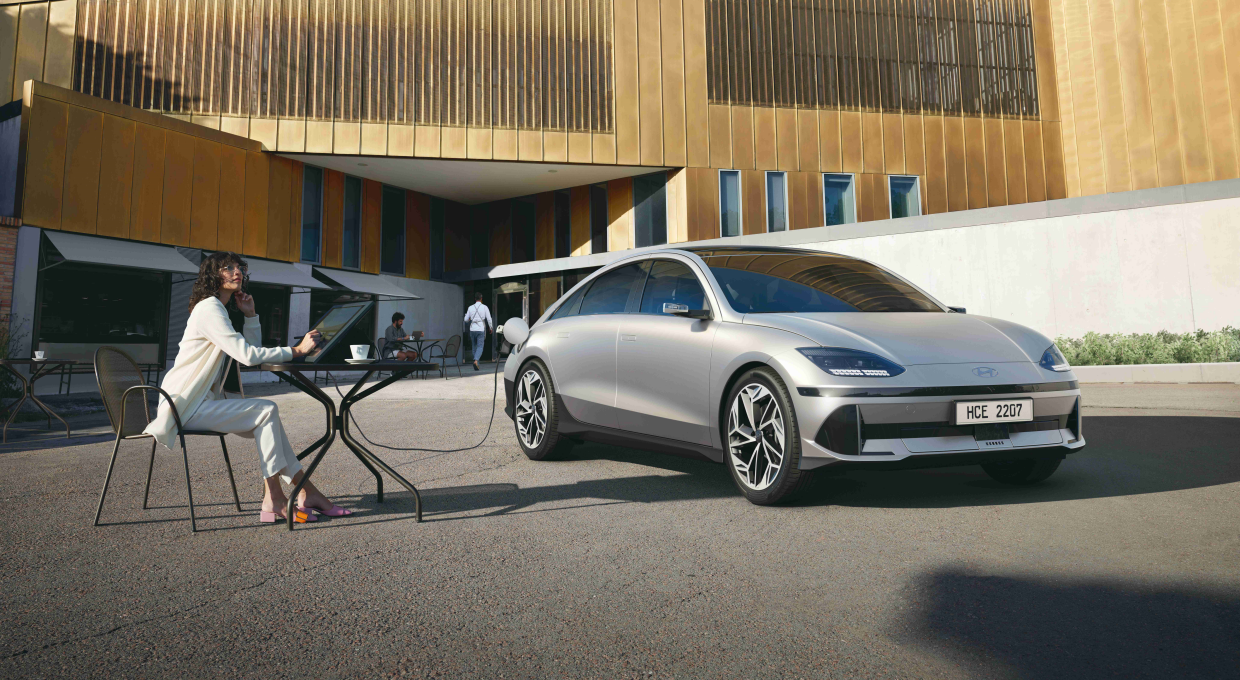 야외 테이블에 앉아 있는 여자와 아이오닉 6 전측면부