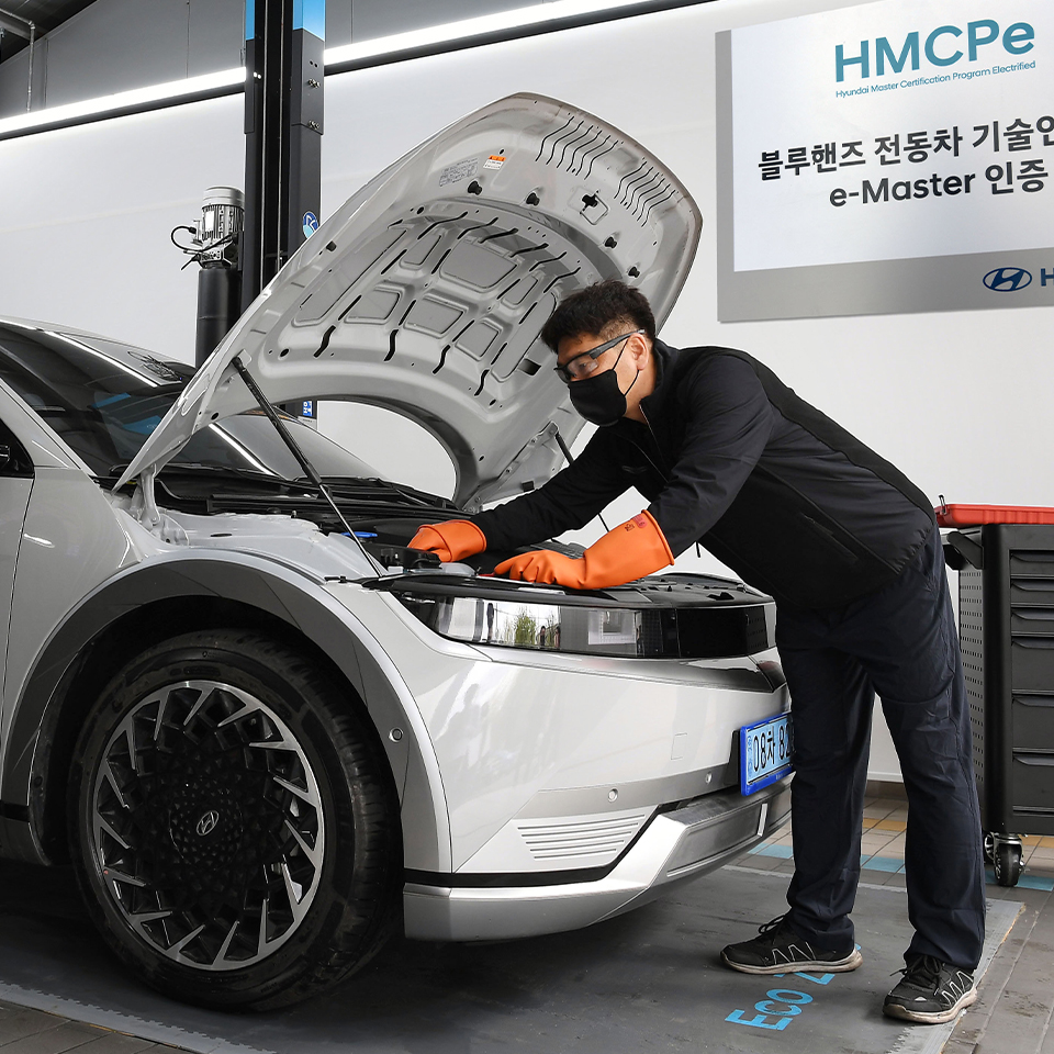 A mechanic is opening the bonnet of an electric car and inspecting the vehicle