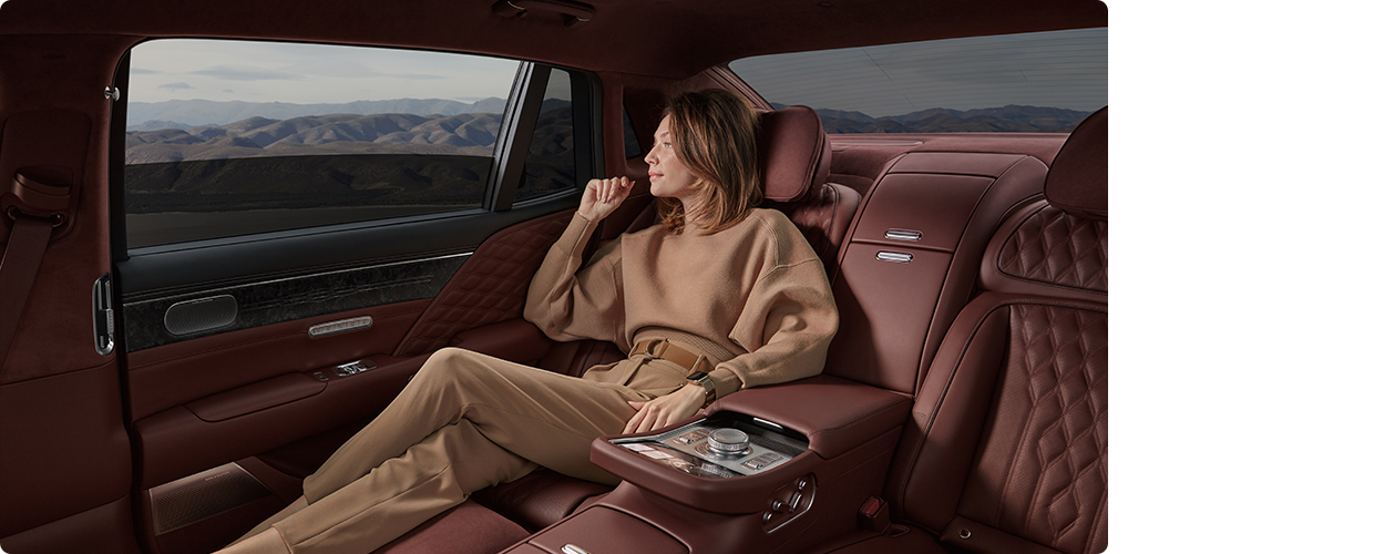 A model is sitting in the backseat of a Genesis G90 and looking out the window