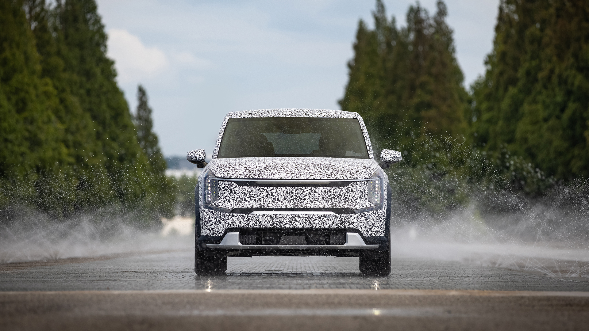 위장막을 쓴 기아 EV9이 젖은 노면을 주행하는 모습