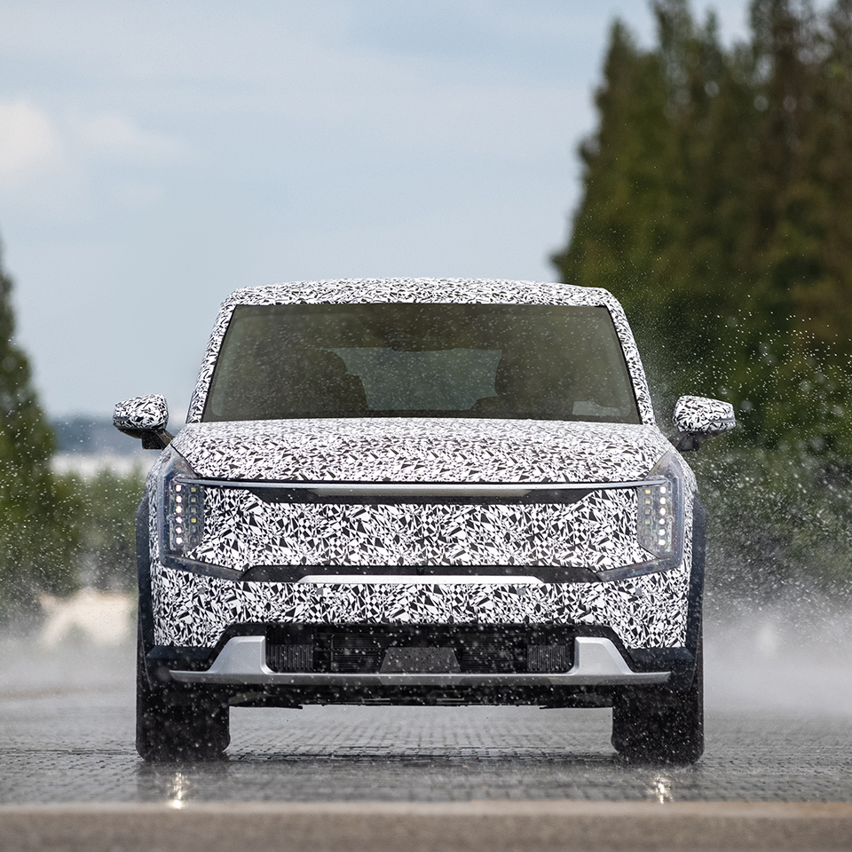 위장막을 쓴 기아 EV9이 젖은 노면을 주행하는 모습