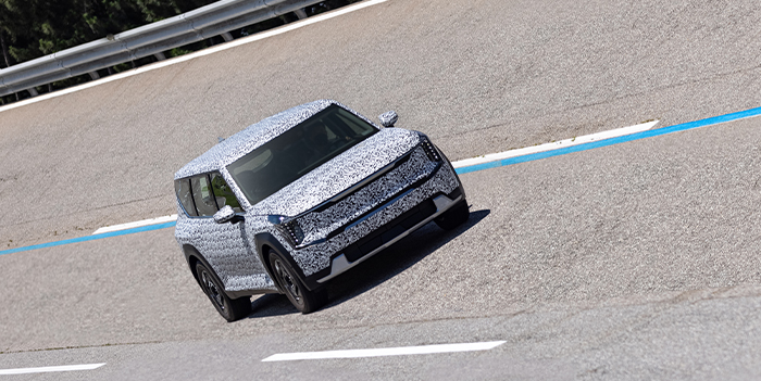 A Kia EV9 in camouflage film driving on a high-speed track