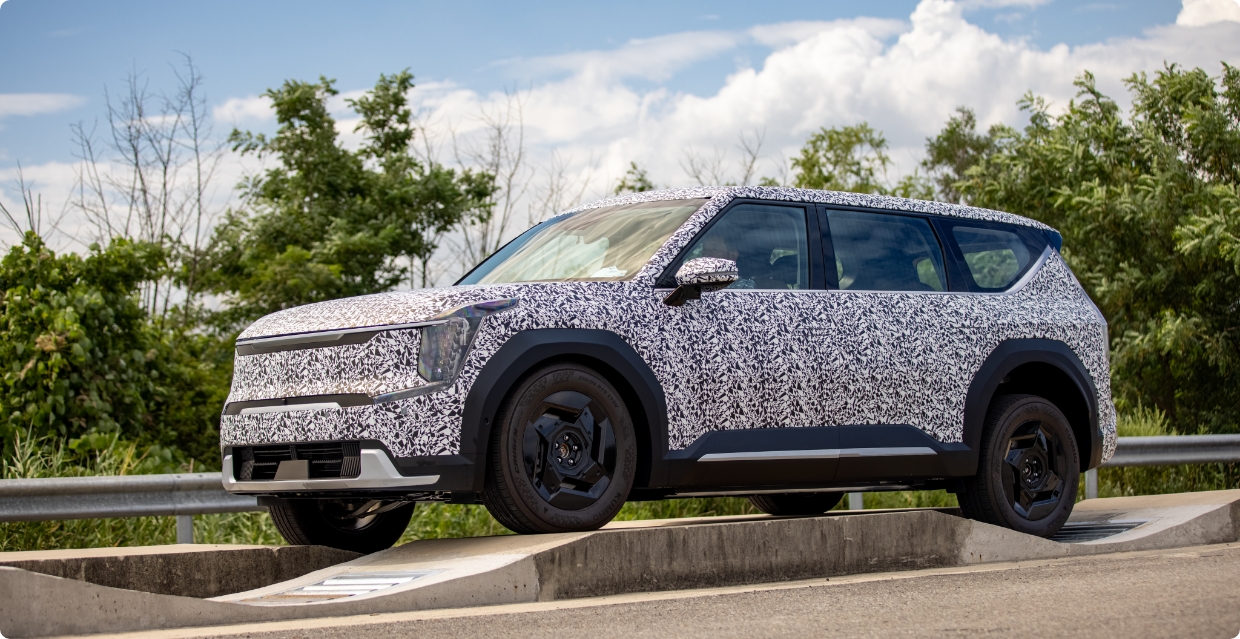 A Kia EV9 in camouflage film driving on a terrain mode test track