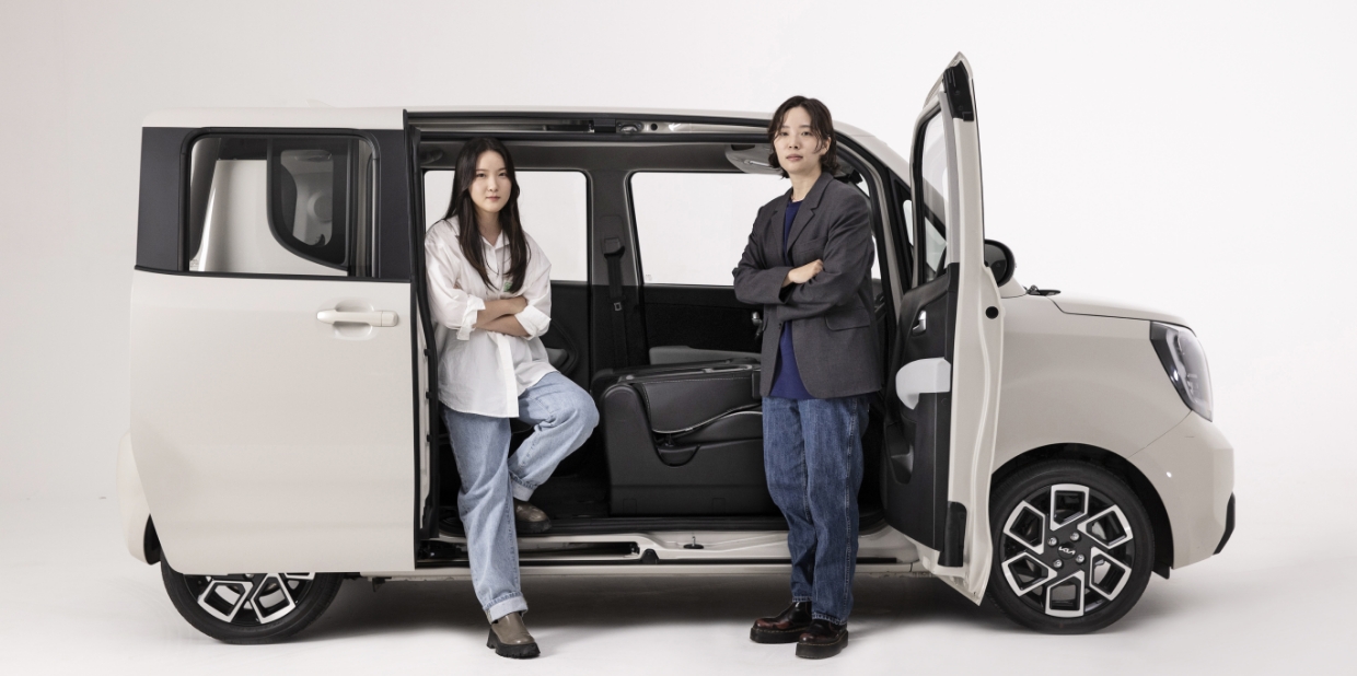 스튜디오에 전시되어 있는 더 뉴 기아 레이가 조수석 도어와 슬라이딩 도어를 열고 두 디자이너가 서 있는 모습