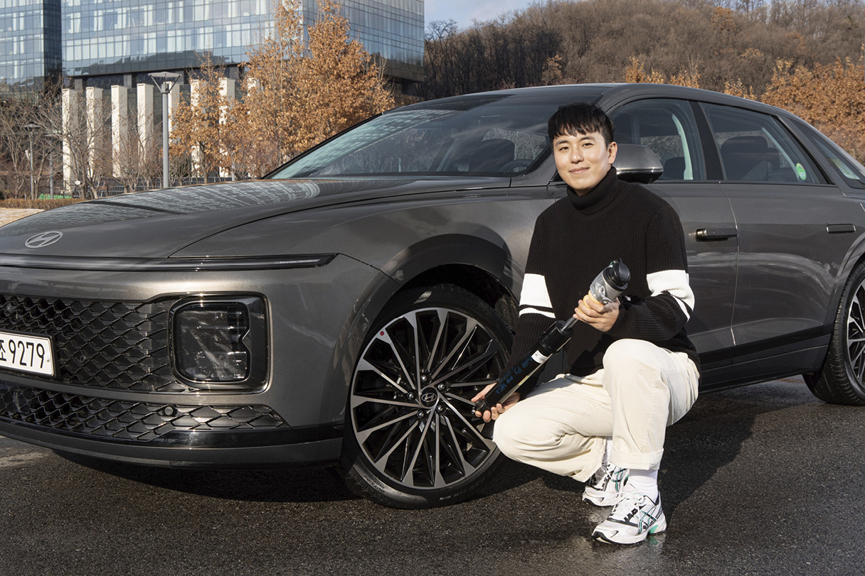 Senior researcher Jeon Kang-wook holding a frequency-sensitive high-performance shock absorber in front of the Grandeur