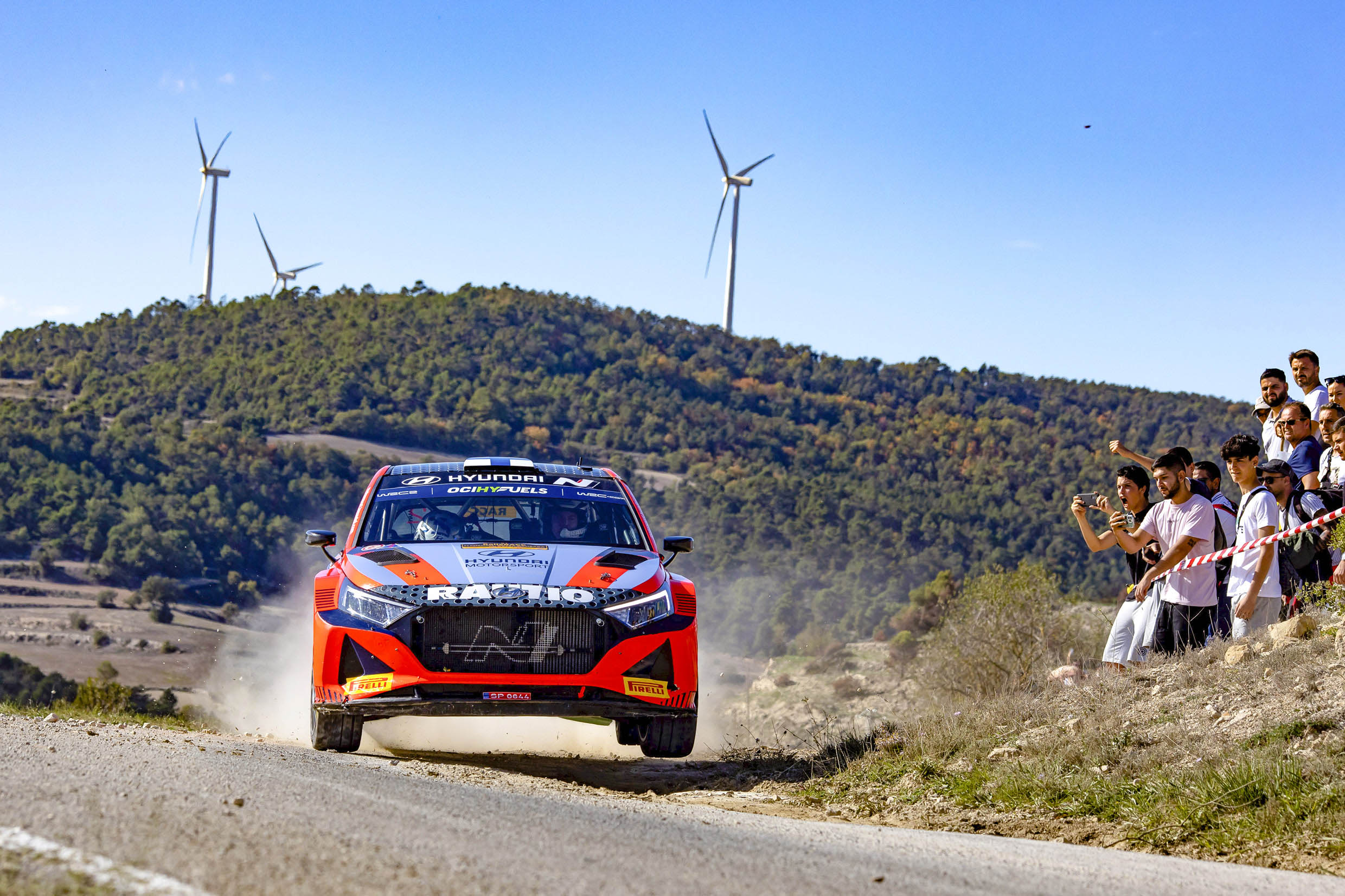 The image of a WRC racing car running while receiving cheers from the crowd