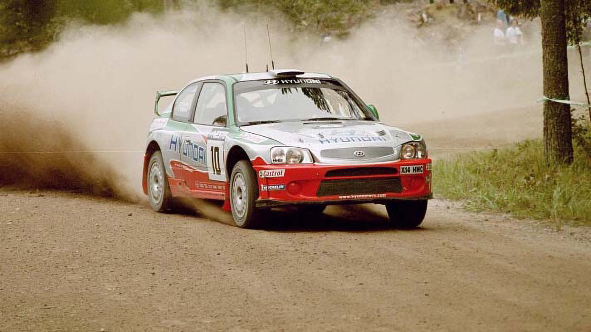 A Hyundai Accent WRC rally car turning a corner with sand dust