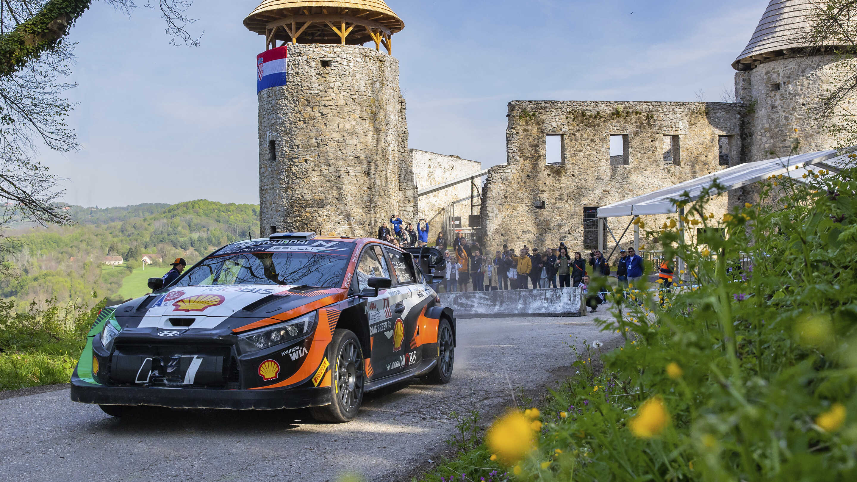 A Hyundai rally car speeding down the road in front of the castle