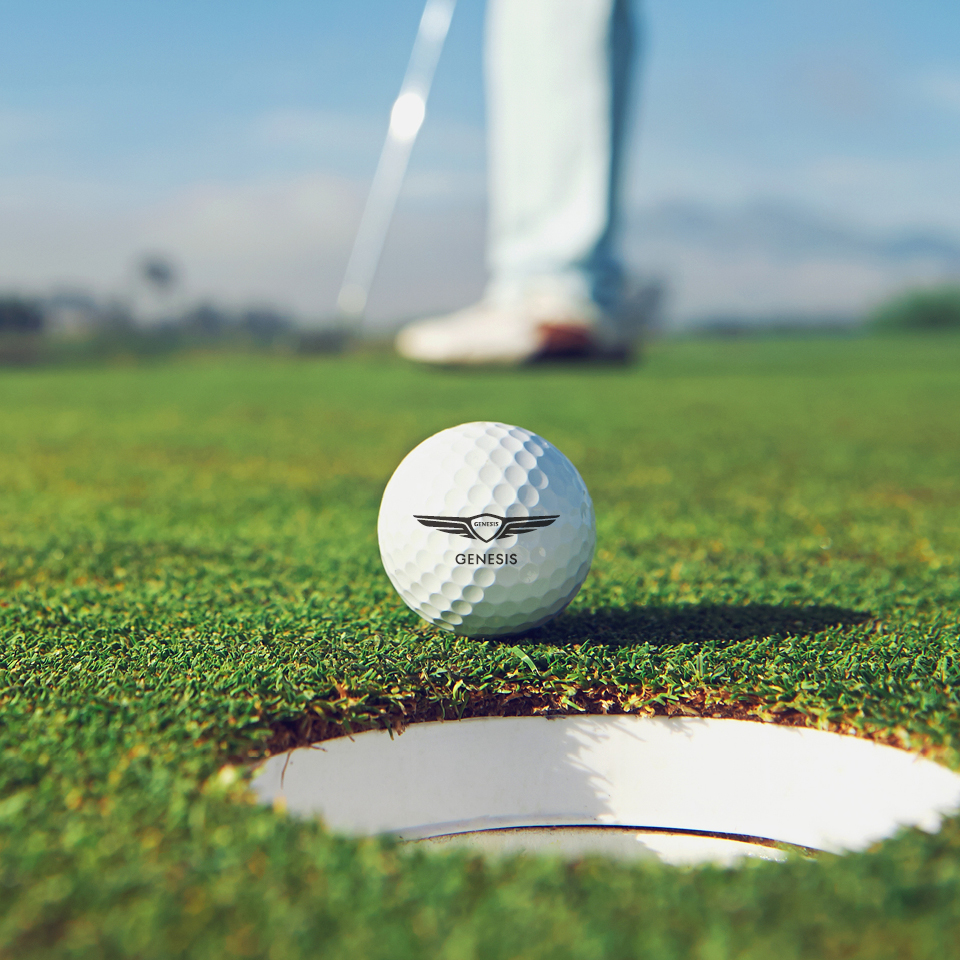 골프 그린 위에서 골프공을 홀컵을 향해 퍼팅하고 있다.