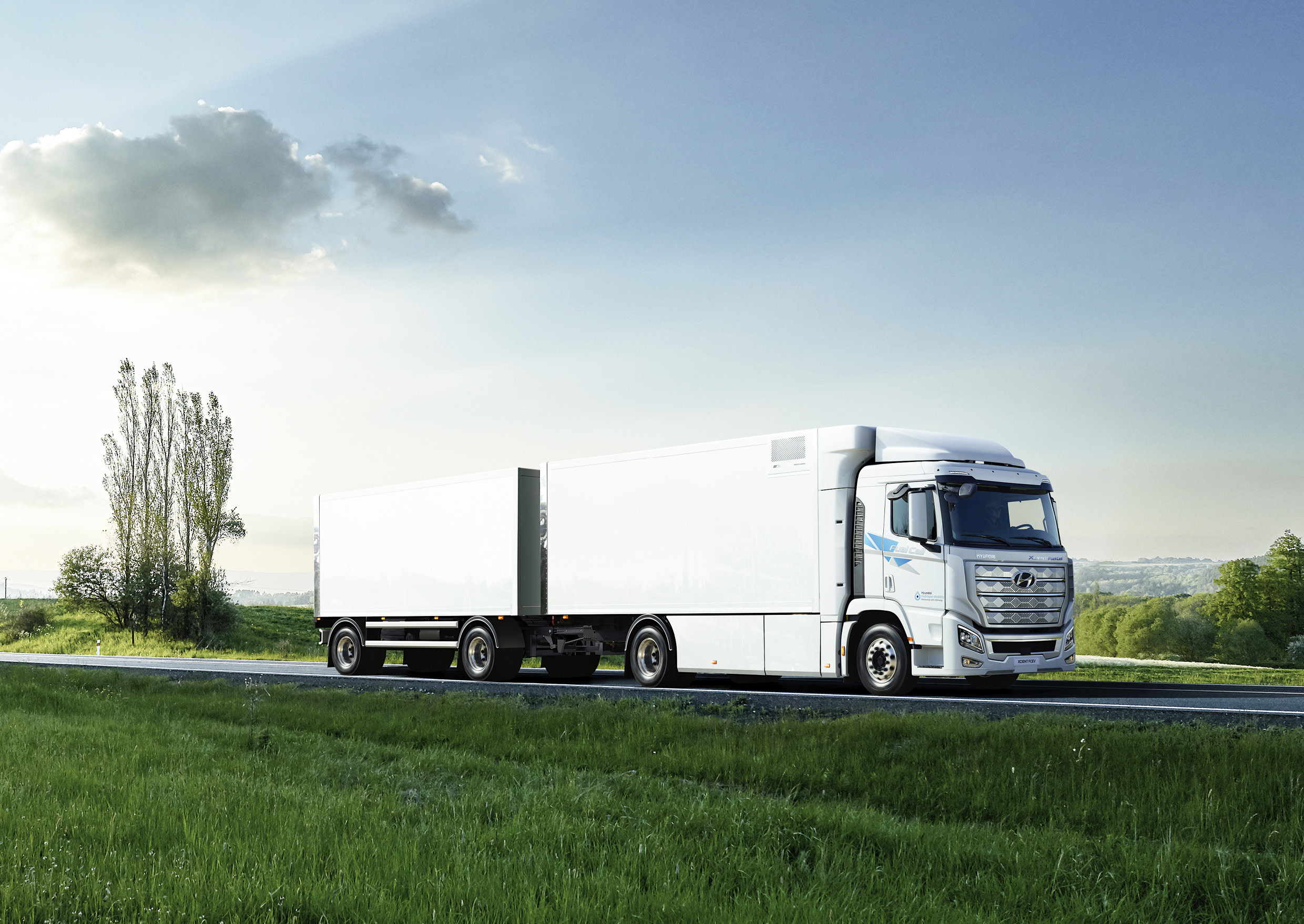 엑시언트 수소전기트럭이 푸른 들판 사이의 길을 달리는 모습