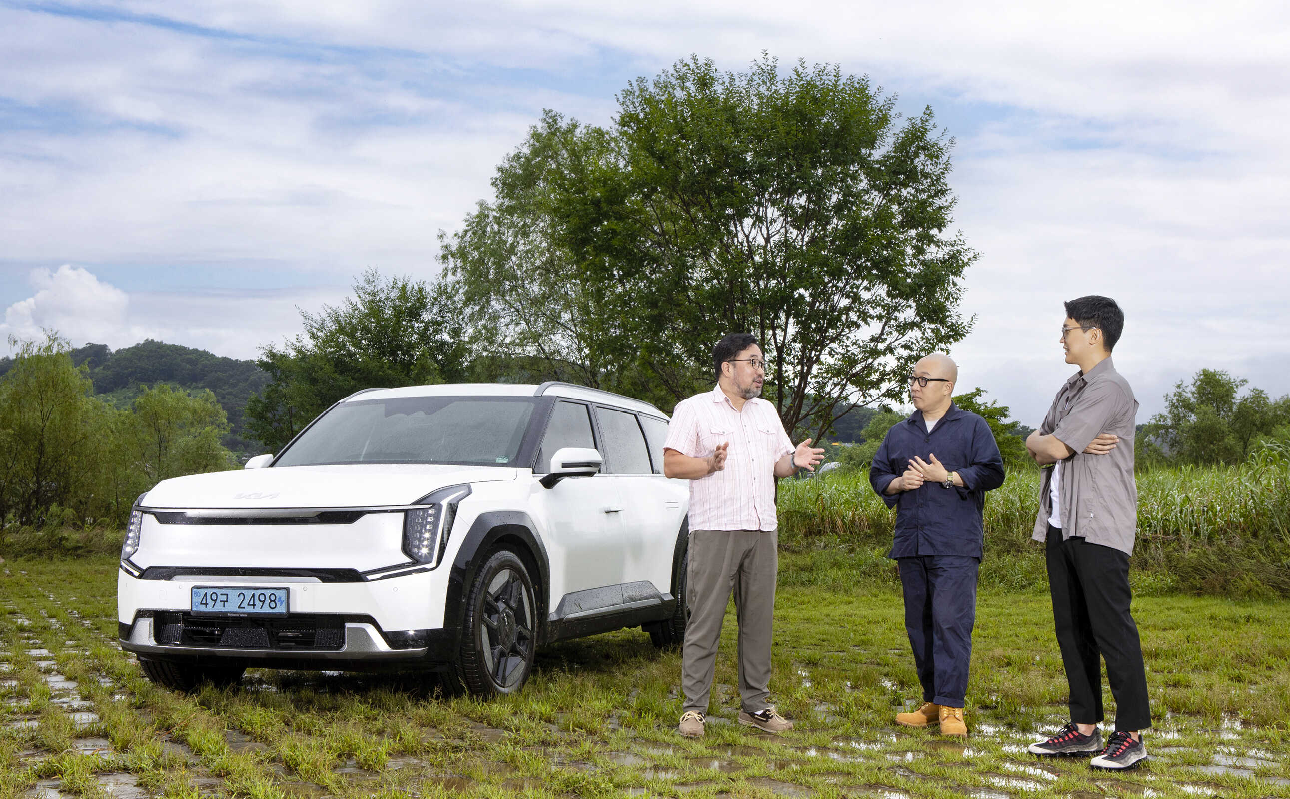 잔디밭에서 선 EV9을 배경으로 세 명의 남자가 대화하는 모습